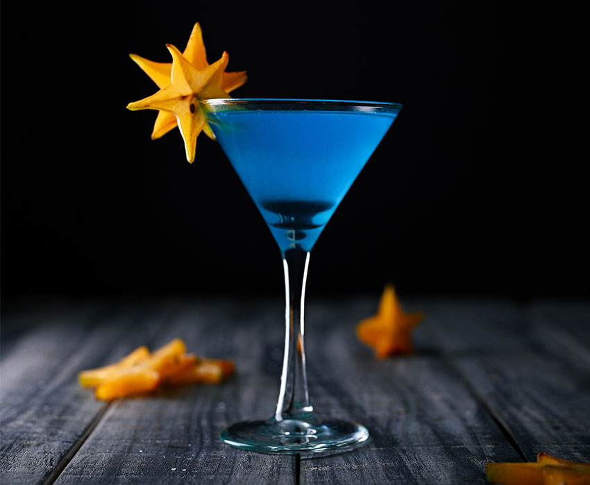 Blaufarbiger Cocktail mit Sternfrucht Karambola dekoriert